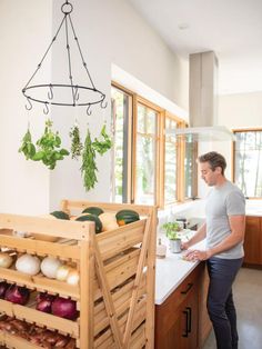 a man standing in front of a kitchen island with vegetables on it and hanging from the ceiling