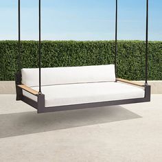 a white couch sitting on top of a wooden swing bed next to a lush green hedge