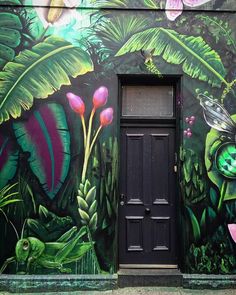 a black door is in front of a colorful wall with flowers and plants painted on it