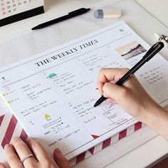 a person is writing on a calendar with a pen and paper in front of them