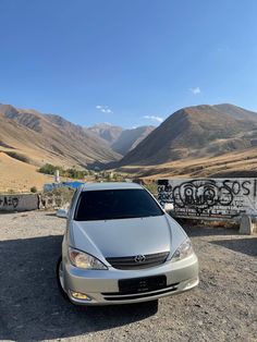 a silver car parked in front of some mountains with graffiti on the wall behind it