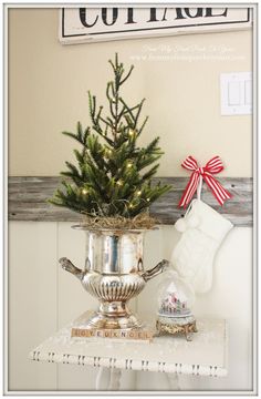 a christmas tree in a silver pot on top of a table with stockings and stockings