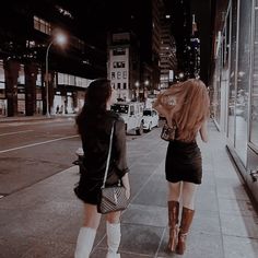 two women walking down the sidewalk in front of a store window at night with their backs to each other