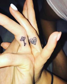 two people with tattoos on their fingers holding each other's hands and one has a key