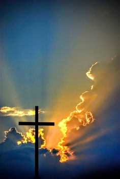 a cross with the sun shining behind it in front of some clouds and blue sky