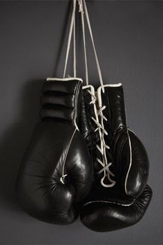 two black boxing gloves hanging from a hook on a gray wall with white laces