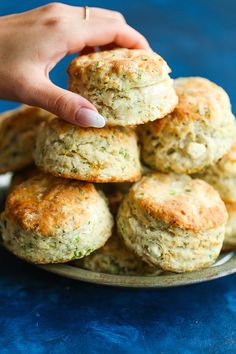 a hand picking up some biscuits from a plate on a blue tablecloth with the rest of the cookies in the background