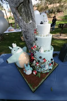 a three tiered cake sitting on top of a blue tablecloth covered park area