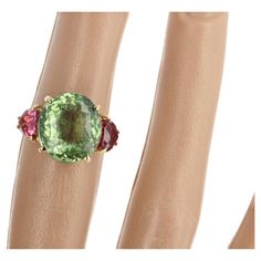 Unique 6 carat sparkling oval green Tourmaline (13 mm x 11.7 mm) enhanced with two glittering pink trillion cut Tourmalines (6 mm x 6 mm approximately) set in an 18 Kt yellow gold handmade ring size 5 (sizable). There are no eye visible inclusions in the large green Tourmaline (in the photos the back of the ring shows through the clear front gemstone due to the lighting for the photograph). Handmade Gold Ring, Gold Cocktail Ring, Gold Cocktail, 18k Yellow Gold Ring, Tourmaline Ring, Green Tourmaline, Pink Tourmaline, Yellow Gold Rings, Cocktail Rings