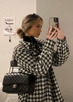 a woman is taking a selfie with her cell phone while wearing a black and white coat