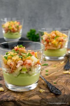 three small glass bowls filled with food on top of a wooden table next to spoons