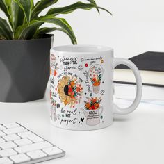 a white coffee mug sitting on top of a desk next to a keyboard and potted plant