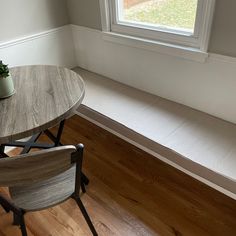 a wooden table with two chairs next to it and a potted plant on the window sill