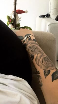 a woman's arm with tattoos on it and flowers in the background, sitting on a couch