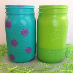 two painted mason jars sitting next to each other on a table with green and purple confetti