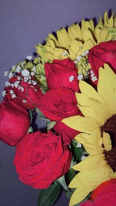 a vase filled with red roses and yellow sunflowers