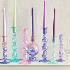 there are many different colored glass candles on the shelf in front of each other with one candle between them