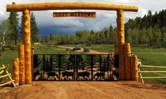 an entrance to a forest with trees and animals on the gate, in front of a dirt road