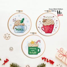 three cross - stitch christmas ornaments with coffee mugs and hot cocoa in them on a white background