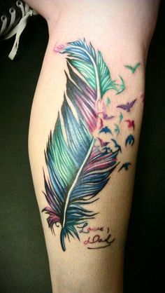 a colorful feather tattoo on the leg with birds flying around it and writing in cursive ink