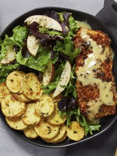 a black plate topped with meat, potatoes and salad