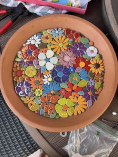 a bowl filled with lots of different colored flowers on top of a table next to scissors