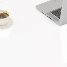 a laptop computer sitting on top of a white desk next to a cup of coffee