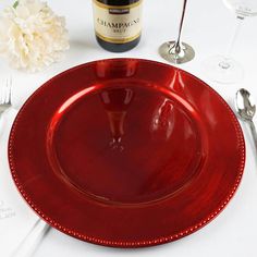 a red plate sitting on top of a white table next to a bottle of wine