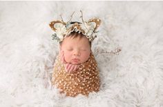 a newborn baby is wearing a deer headband and laying on a white blanket with her hands under her chin