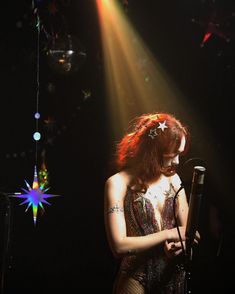 a woman standing in front of a microphone on stage with lights shining down behind her