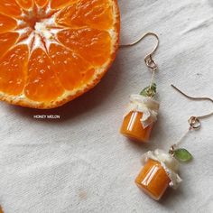 an orange slice and some silver earrings on a white cloth with a piece of fruit in the background