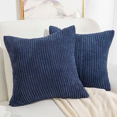 two blue pillows sitting on top of a white couch next to a cup and saucer