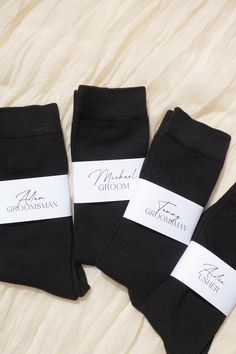 three pairs of black socks with white labels on them, sitting on a bed sheet