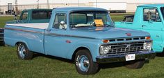 an old blue truck parked on top of a grass covered field next to other trucks