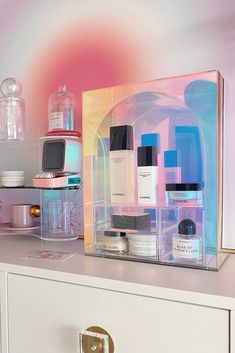 an assortment of skin care products displayed on top of a white dresser with pink and blue background