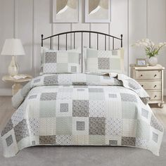 a bed with a white and grey quilt on it's coverlet next to a night stand