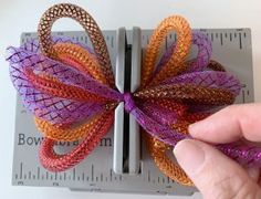 a hand is holding a purple and orange bow on top of a measuring ruler,