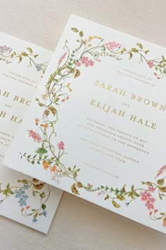 two wedding cards with floral designs on the front and back, sitting next to each other