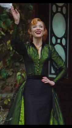 a woman in a green and black dress is waving to the side with her hand up