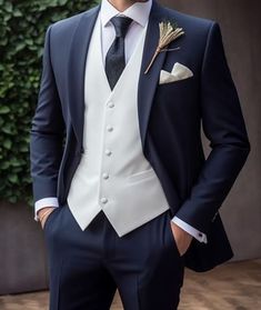 a man wearing a suit and tie standing in front of a wall with greenery