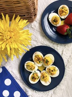 two plates with deviled eggs and strawberries on them next to a basket of flowers