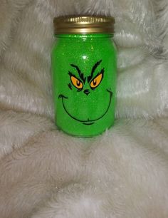 a green mason jar with an evil grin face painted on the front and yellow eyes