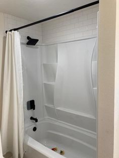 a white bath tub sitting inside of a bathroom next to a shower curtain with black handles