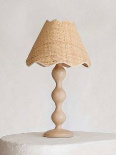 a table lamp sitting on top of a white pedestal with a beige shade over it