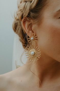 a woman wearing large gold earrings with pearls on the bottom and sunbursts at the top