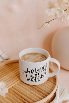 a cup of coffee sitting on top of a wooden tray next to a white flower