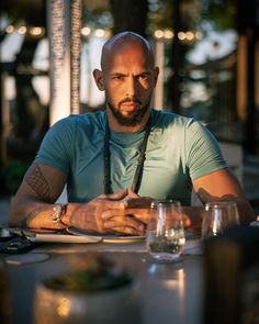 a bald man sitting at a table with wine glasses in front of him and looking to the side