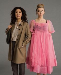 two women standing next to each other in dresses and coats, one wearing a pink dress