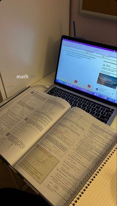 an open book sitting on top of a laptop computer next to a notebook and pen