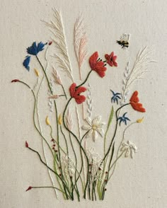 embroidered flowers and grass on white linen with two bees flying in the sky behind them